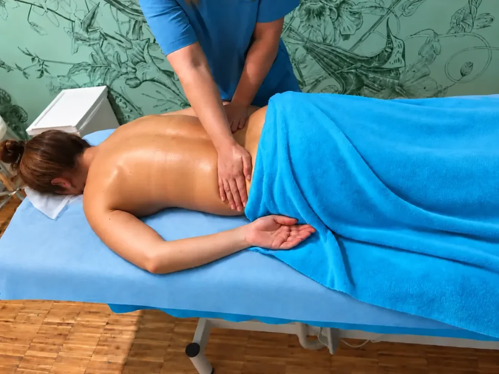 Hands massage the back of a relaxed client lying under a turquoise towel.